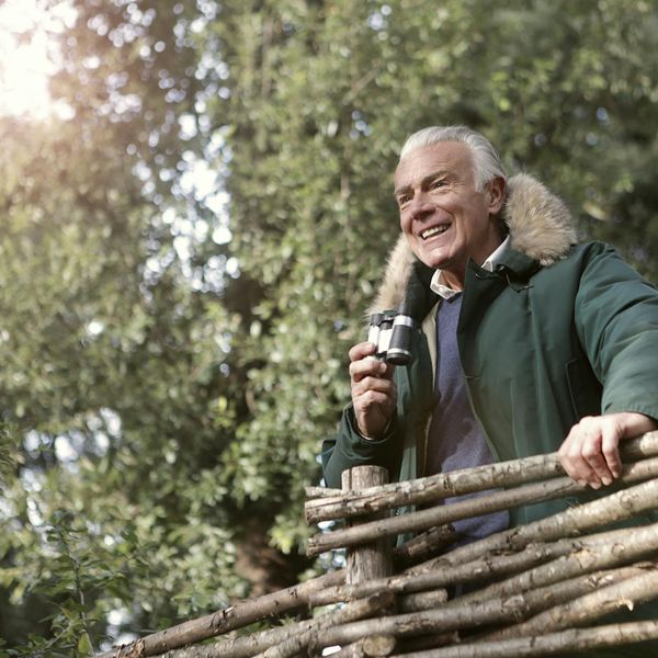 Smiling senior man stretching outdoors in a green park.